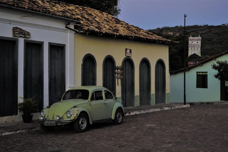 Casas coloniais coloridas com portas em arco e um Fusca verde estacionado na rua de pedra