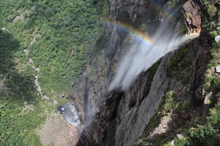Água da cachoeira virando névoa, com um arco-íris diante do paredão