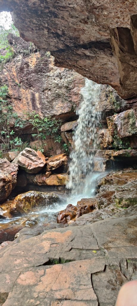 Cachoeira descendo pelas rochas sob uma laje de pedra saliente