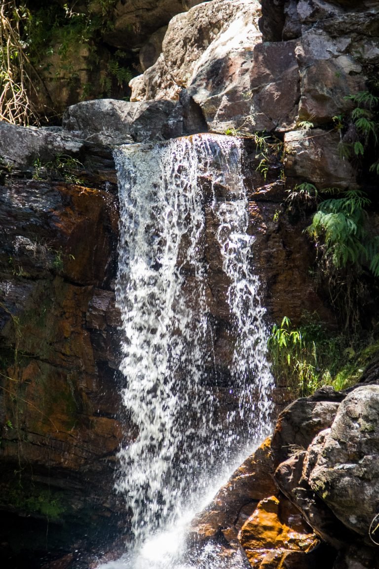 Cachoeira estreita caindo entre rochas escuras e vegetação