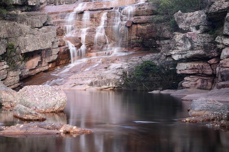 Cachoeira em degraus de rocha rosada caindo em poço de água parada