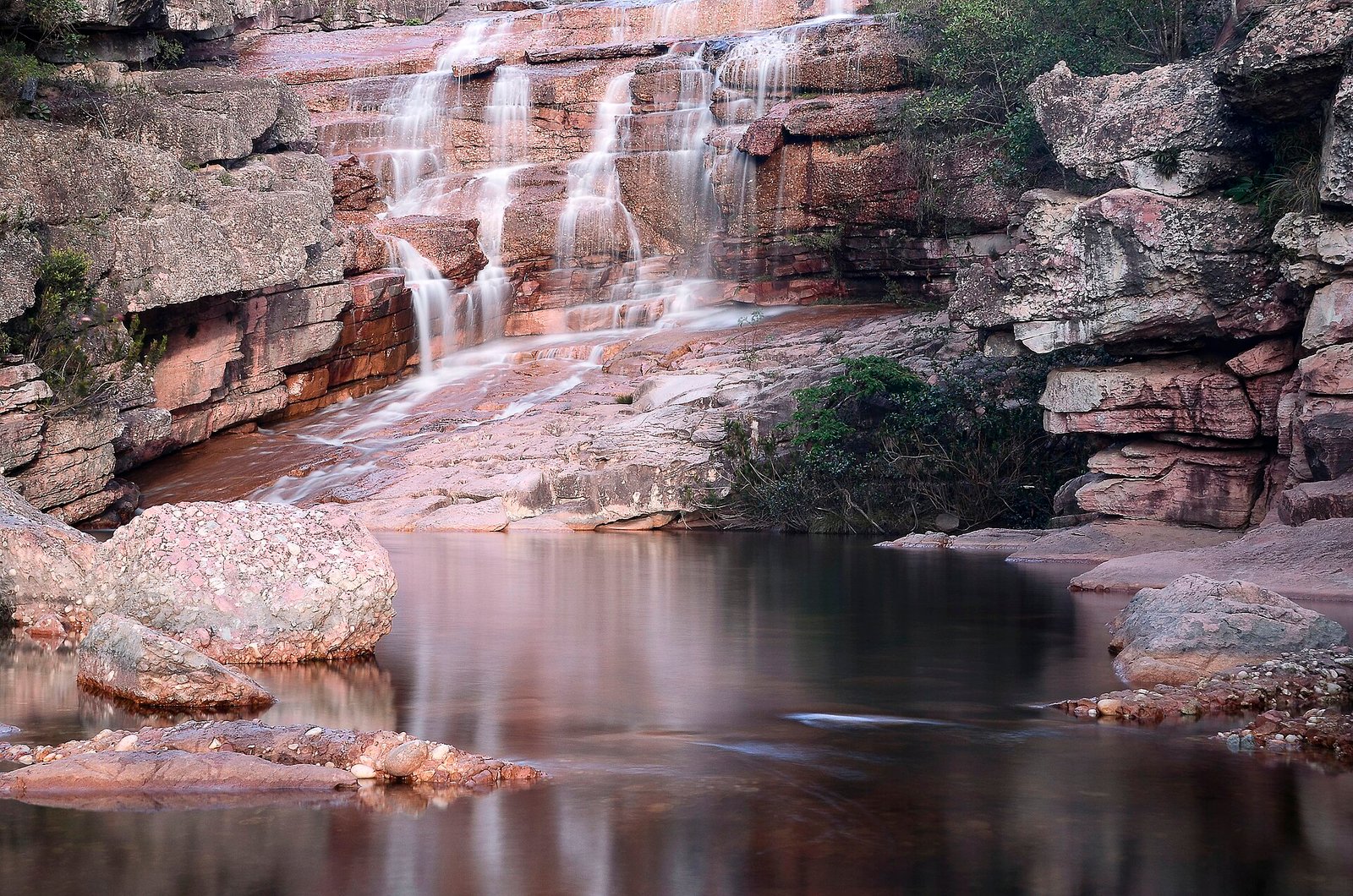 Cachoeira em degraus de rocha rosada caindo em poço de água parada