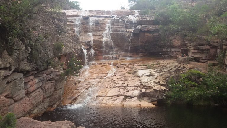 Queda d'água larga escorrendo por lajes de pedra até o poço