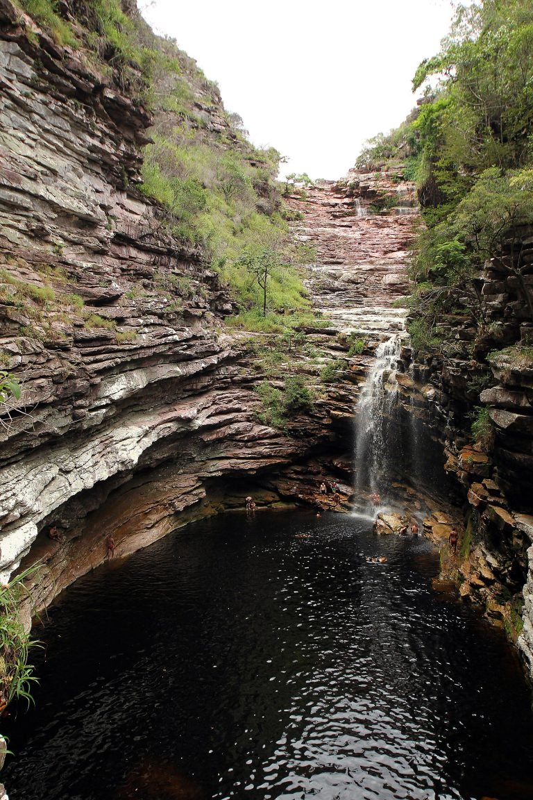 Cachoeira estreita no fundo de cânion com paredões de rocha e poço escuro