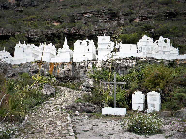 Túmulos brancos em estilo bizantino alinhados na encosta rochosa, com caminho de pedra em primeiro plano