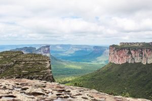 Vale verde entre paredões de arenito e morros de topo plano, visto do alto do Morro do Pai Inácio sob céu com nuvens