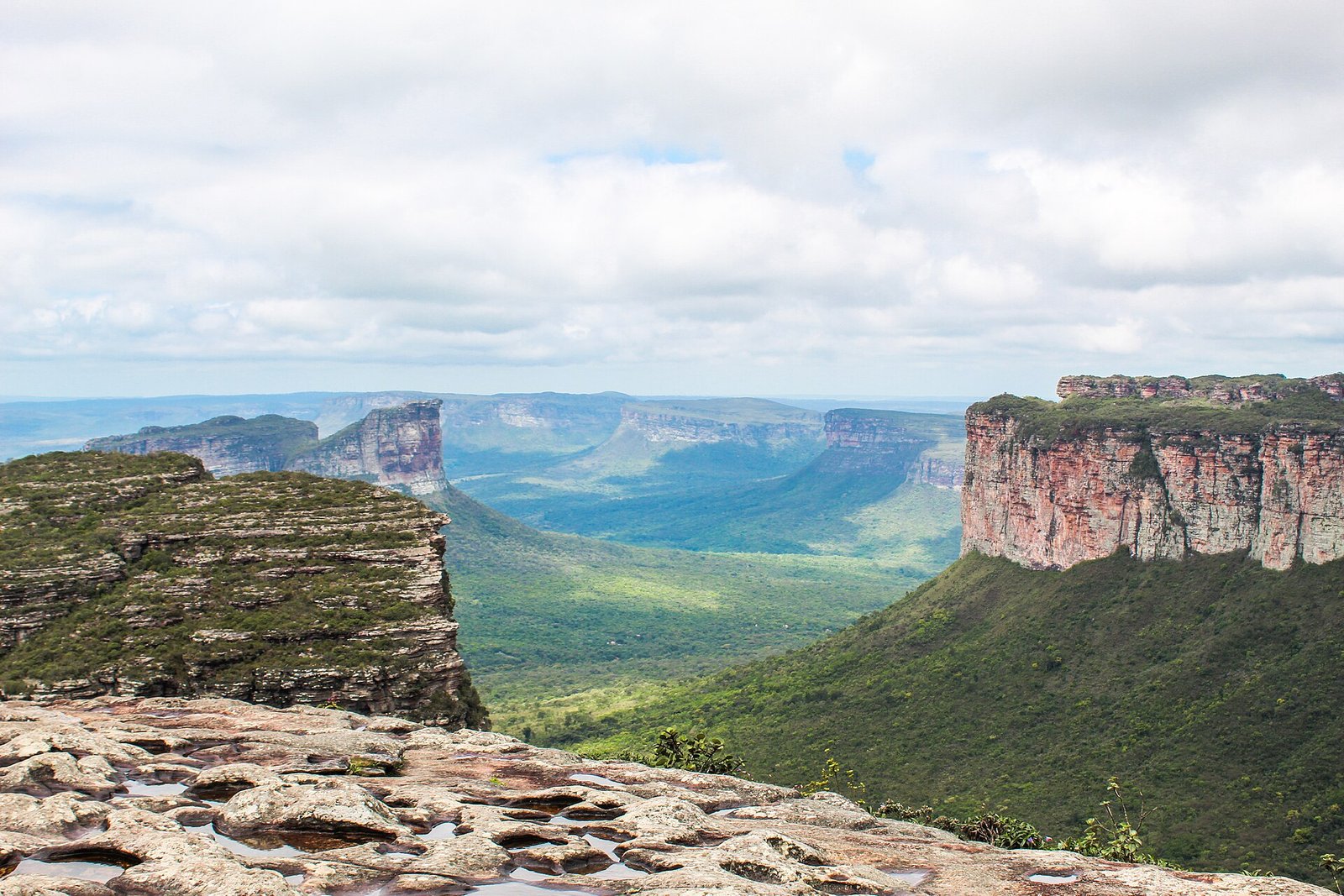 Vale verde entre paredões de arenito e morros de topo plano, visto do alto do Morro do Pai Inácio sob céu com nuvens