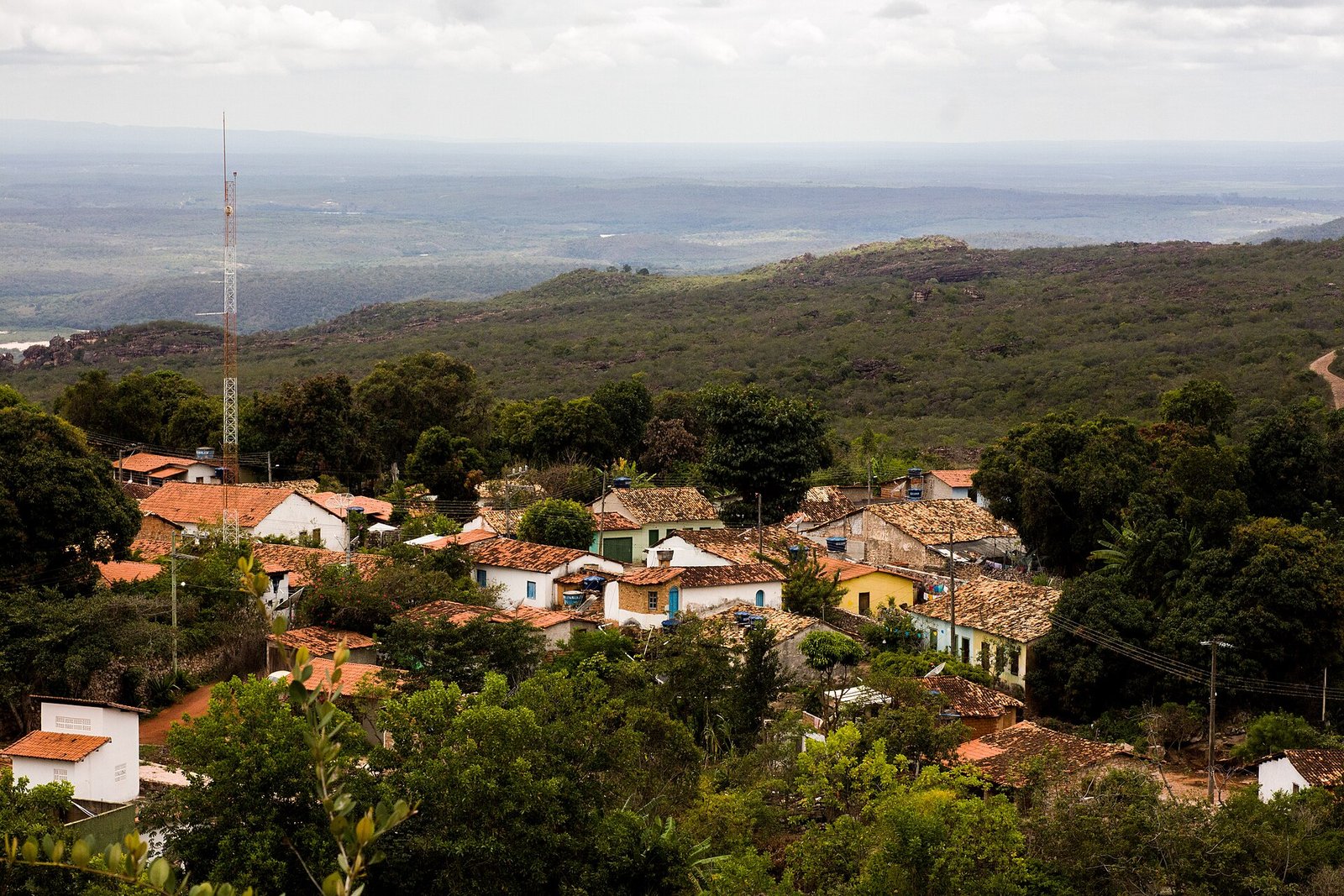 Casario de Igatu com telhados cerâmicos entre a mata, com planície ao fundo