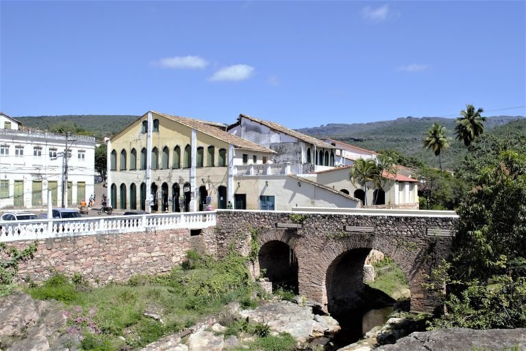 Ponte de pedra em arcos sobre o rio Lençóis, com casarões coloniais ao fundo e serra no horizonte