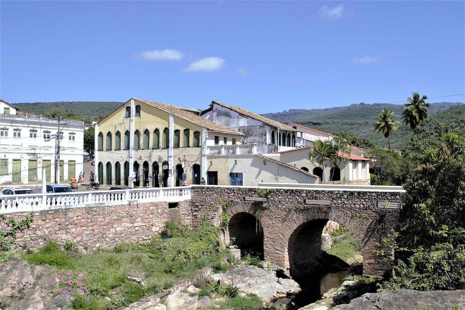 Ponte de pedra em arcos sobre o rio Lençóis, com casarões coloniais ao fundo e serra no horizonte