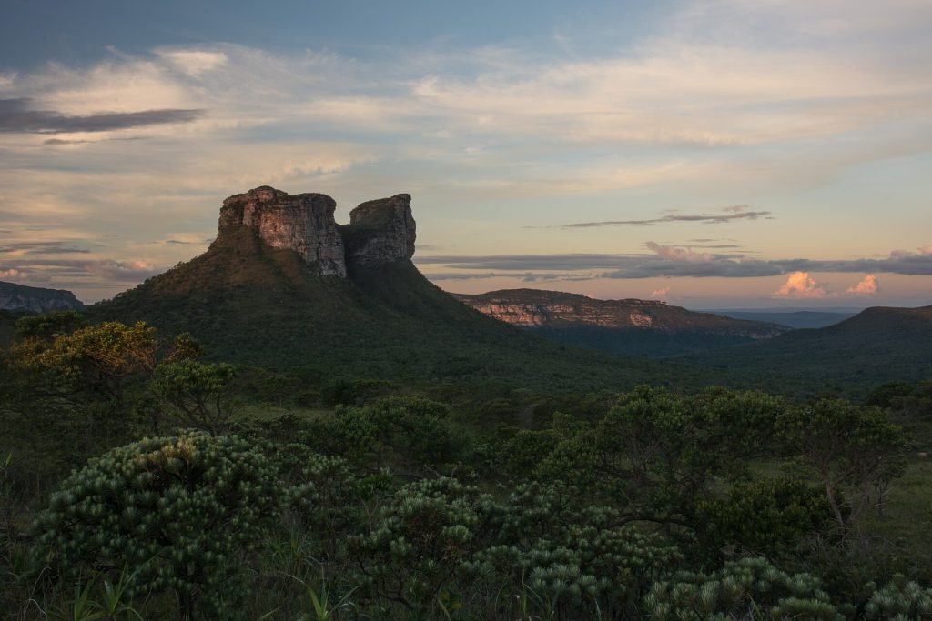 Silhueta do Morro do Camelo no horizonte com céu de fim de tarde e vegetação em primeiro plano