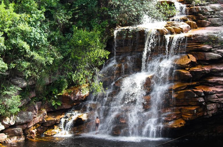 Cachoeira larga entre rochas avermelhadas e vegetação