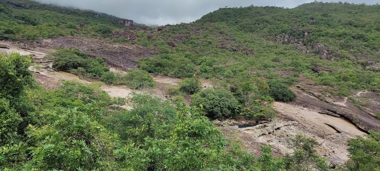 Leito de pedra do rio Serrano com poços naturais entre a vegetação, aos pés da serra