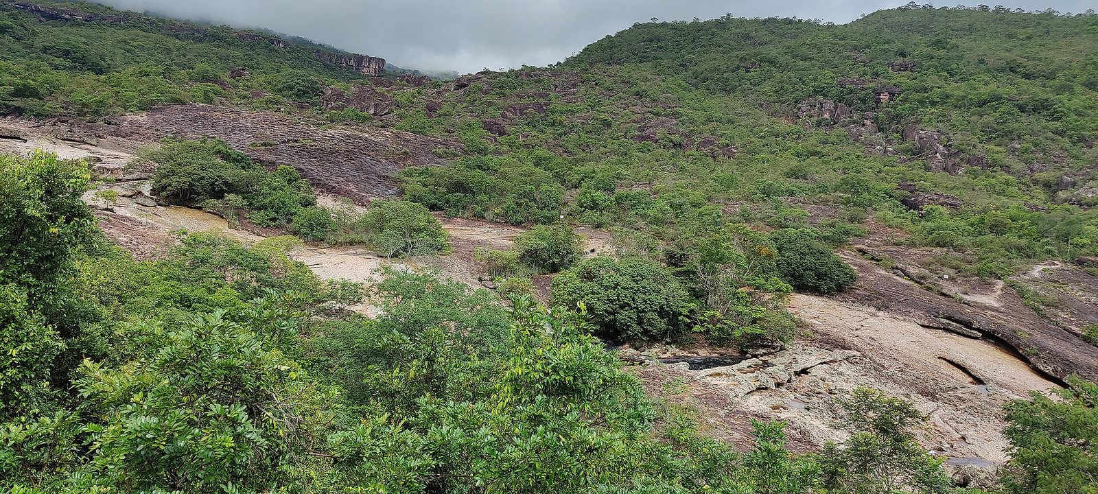 Leito de pedra do rio Serrano com poços naturais entre a vegetação, aos pés da serra