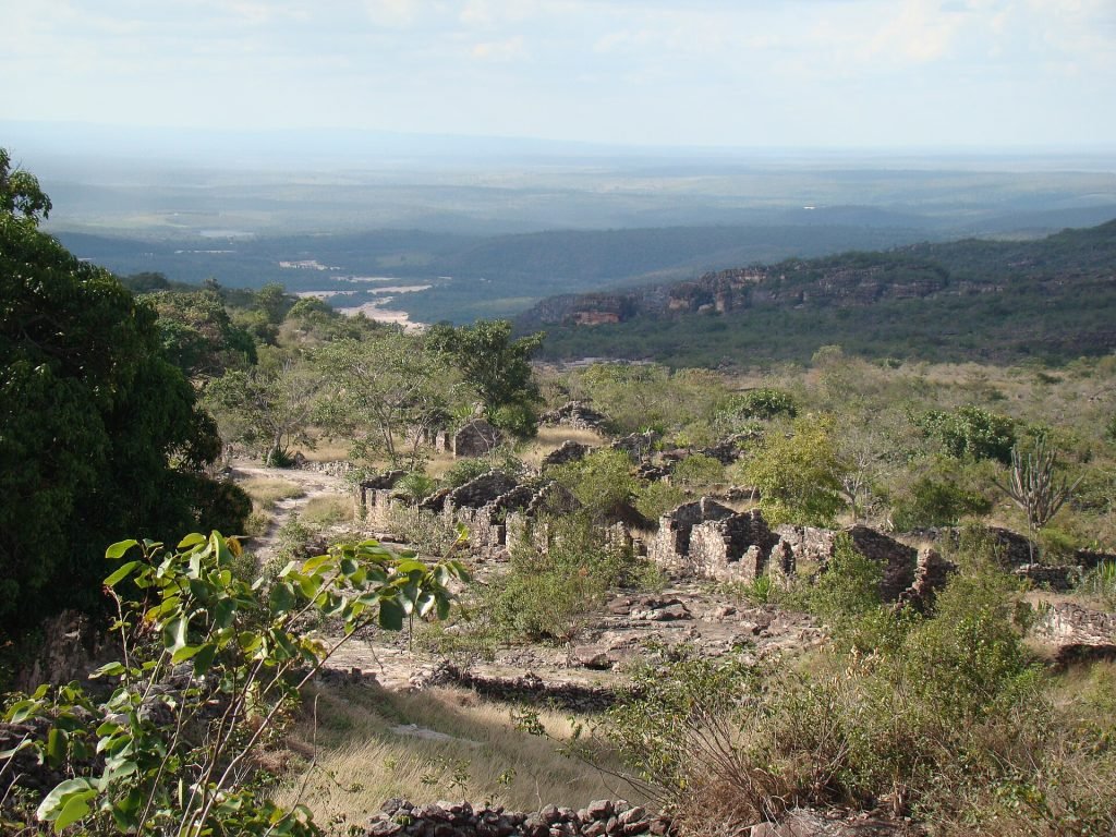 Restos de muros de pedra espalhados na encosta, com vale e serras ao fundo