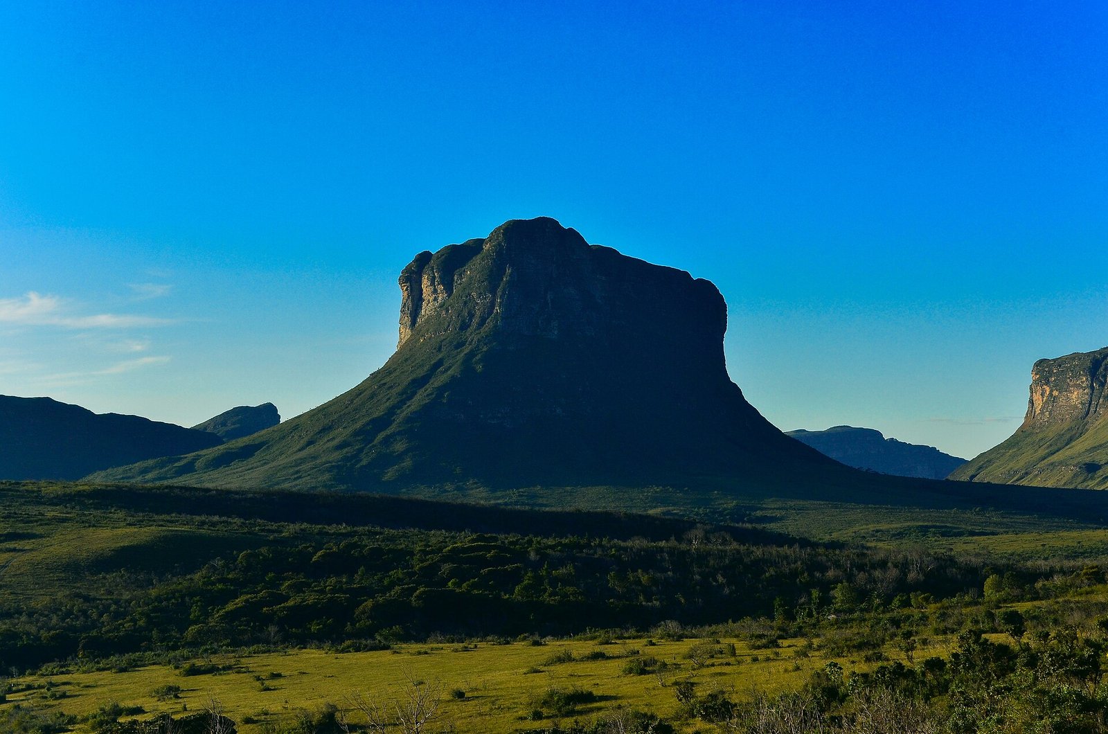 Morrão, grande morro de paredões rochosos, iluminado pelo sol sobre vale verde
